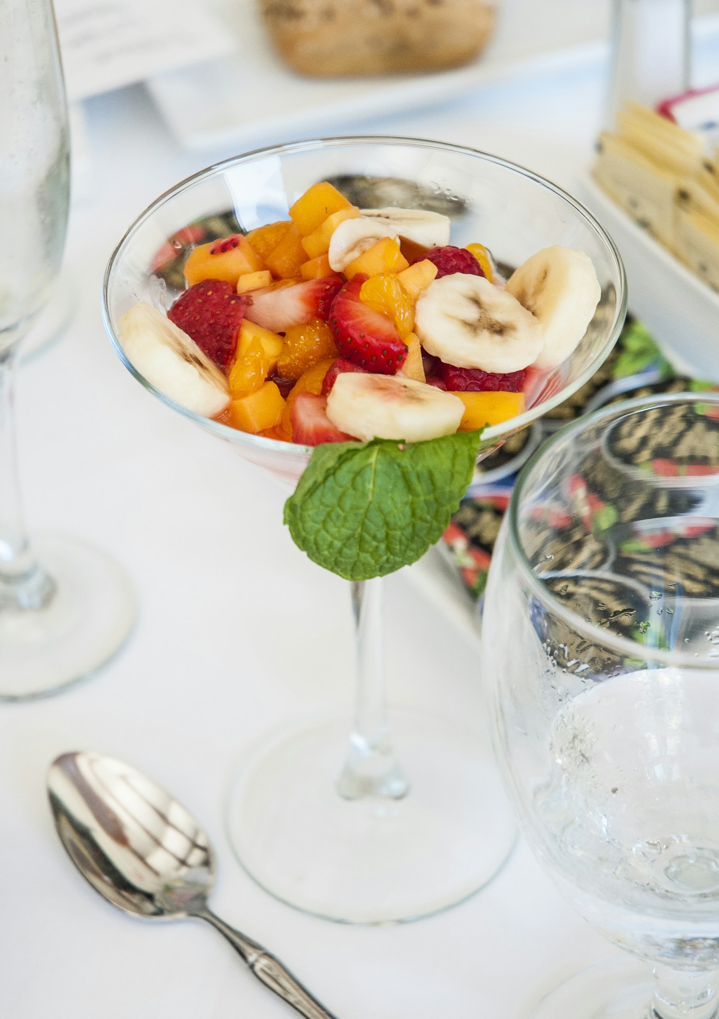 A bowl of fruit and a glass of water on a breakfast table